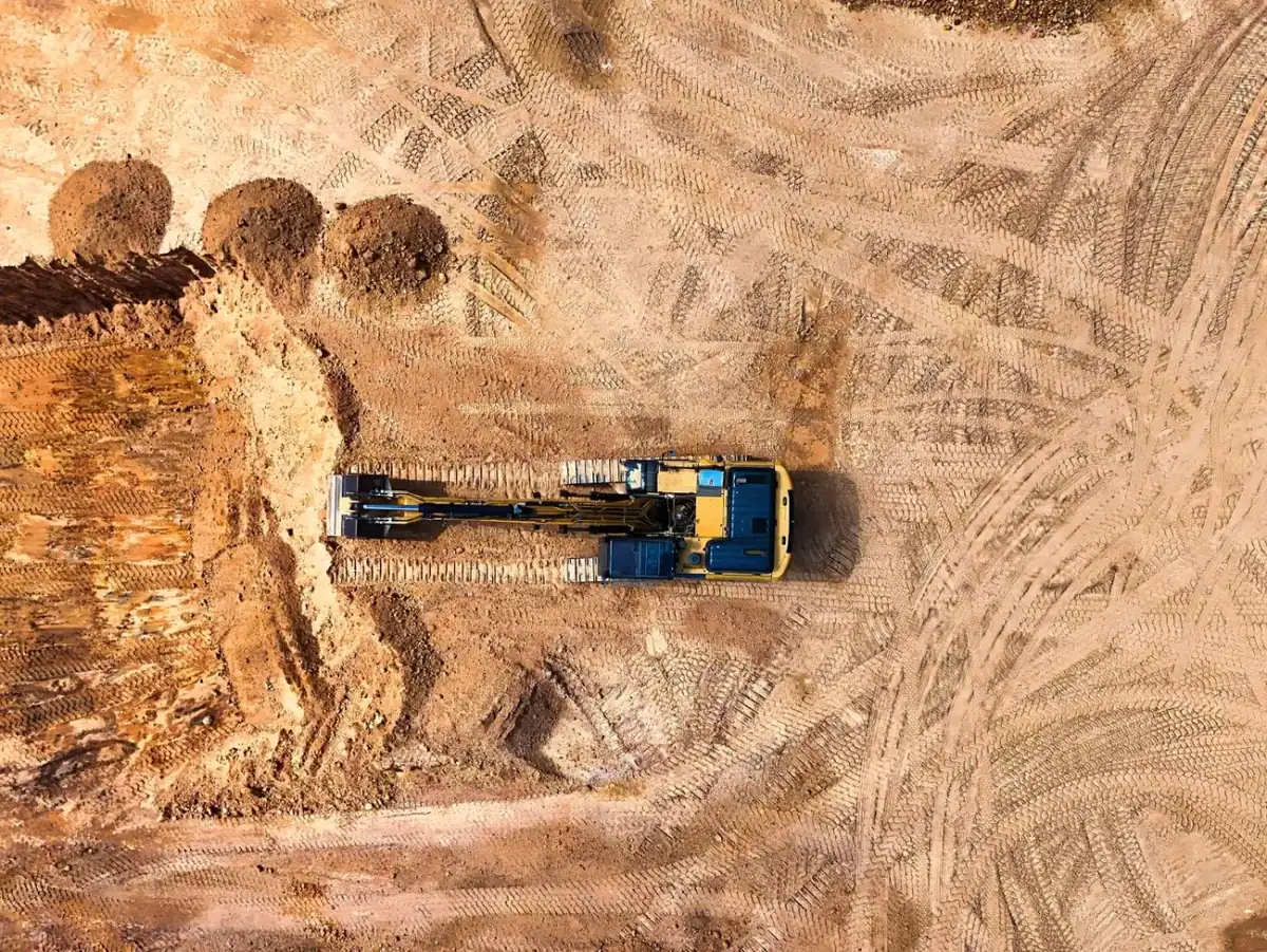 Vue aérienne d'une pelle mécanique à chenilles sur un terrain décapé, traces de chenilles et tas de terre